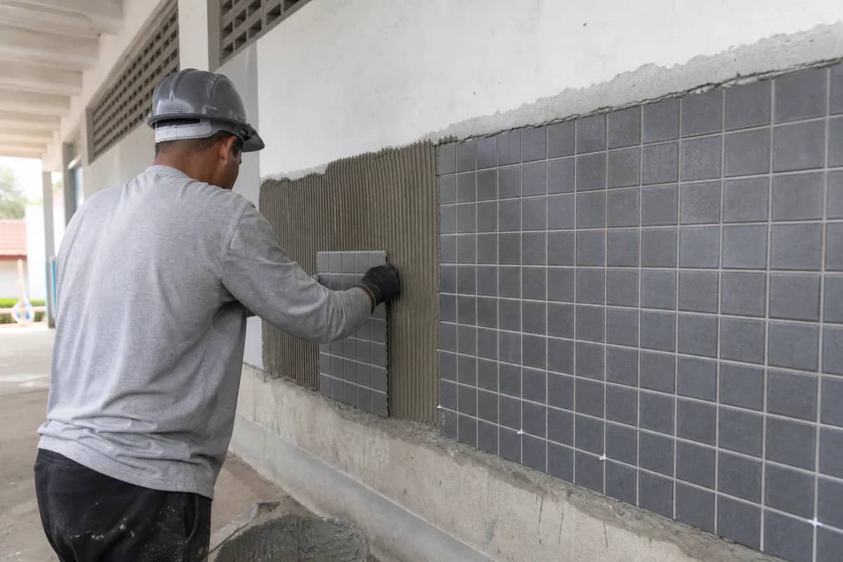 Profissional instalando revestimento cerâmico em parede de escola