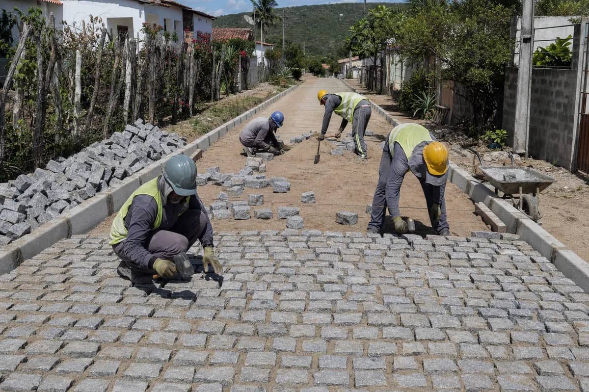 Equipe assentando paralelepípedos graníticos entre meios-fios em uma via rural de Mogeiro